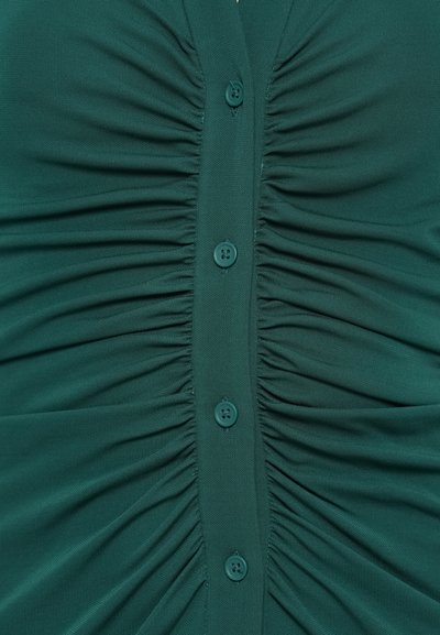 Zelený vrúbkovaný top s výstrihom do V a piatimi zladenými gombíkmi vpredu, s hladkou textúrou a jemným elastickým efektom.