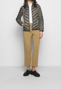 Veste en duvet matelassée avec un motif en chevrons noir et blanc, associée à un pantalon beige ajusté et des mocassins noirs.