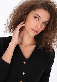 Czarny dzianinowy kardigan z dekoltem w kształcie litery V, z pięcioma złotymi guzikami z przodu i ściągaczami na mankietach. Miękka struktura i staranne szycie.