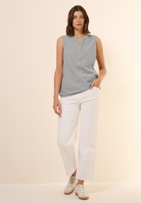 Haut sans manches gris et blanc à rayures avec un décolleté en V, associé à un pantalon large blanc et des baskets de couleur claire. Texture de tissu lisse.