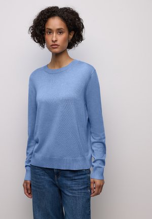 Pull en maille bleu clair avec un col rond, des poignets et un ourlet côtelés. Associé à un jean en denim bleu foncé, ample. Texture lisse.