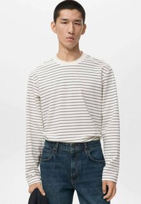 Weißes Langarmhemd mit schwarzen horizontalen Streifen; kombiniert mit dunkelblauen Jeans. Schlichtes, lässiges Design ohne zusätzliche Akzente.