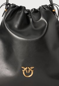 Zwarte leren emmer tas met een gathered bovenkant. Kenmerkt zich door een gouden accent met twee vogelontwerpen en een cirkelvormig hardwaredetail.