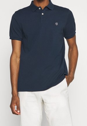 Polo azul marino de tela de algodón, con cuello clásico y un logo sutil en el pecho izquierdo, combinado con pantalones a rayas.