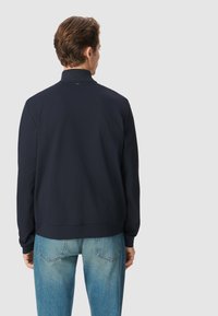 Felpa blu navy con colletto alto, realizzata in tessuto morbido. Presenta maniche lunghe e orlo a costine, abbinata a jeans azzurri.