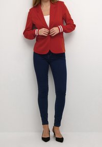 Rød blazer med hvide stribede manchetter, skræddersyet pasform, to forlommer, kombineret med mørkeblå skinny jeans og sorte hæle. Glat tekstur.