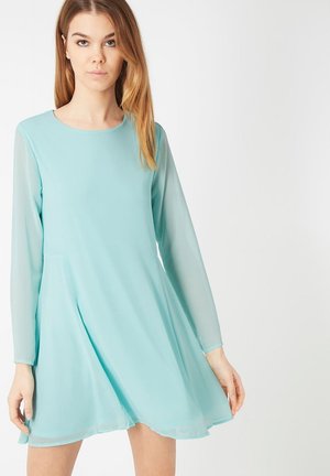 Un vestido azul claro con mangas largas y translúcidas y un escote redondo. Tiene una forma fluida y una textura suave y lisa.