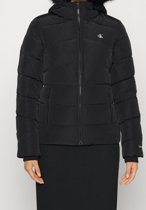 Veste d'hiver noire matelassée avec capuche, fermeture éclair avant, poches latérales zippées et logo blanc "cK" sur la poitrine.
