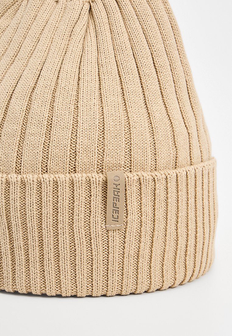 Beżowa czapka beanie z prążkowanej dzianiny, z podwiniętym brzegiem i małą skórzaną metką, z teksturowanym wzorem na całej powierzchni.