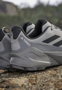 Grijze wandelschoenen met een texturen bovenkant, zwarte accenten en een opvallend logo. Beschikt over een robuuste zool met een onderscheidend ontwerp voor tractie.