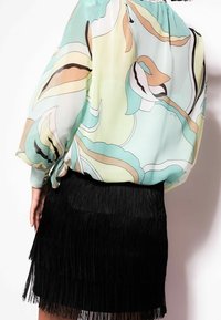 Langærmet, lysegrøn bluse med abstrakt blomsterprint, parret med en sort frynse mini nederdel. Blusen har en afslappet pasform og samlet halsudskæring.