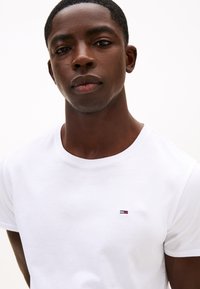 Vit bomulls-T-shirt med rundad halsringning och en liten, broderad logotyp på bröstet. Slät textur, figursydd design.