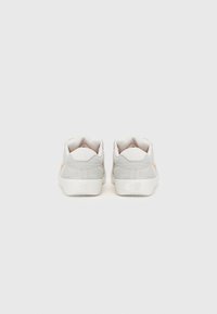 Pari valkoisia ja vaaleanharmaita Nike SB -tennareita kuvattuna takaa yksinkertaisella harmaalla taustalla.
