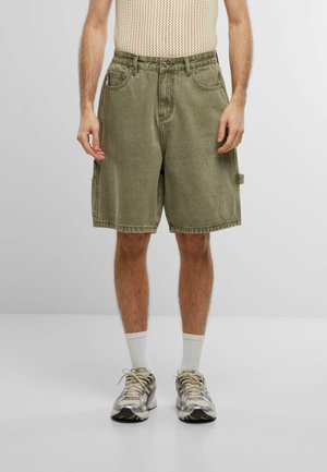 Șorturi din denim de culoare verde măsliniu, cu o croială lejeră, cusături vizibile și buzunare frontale. Purtați cu un top din plasă crem și adidași.
