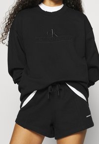 Černá mikina s vyraženým logem "Calvin Klein Jeans", doplněná černými šortkami s bílými bočními akcenty a šňůrkovým pasem.