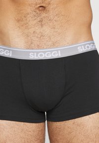 Črni bombažni bokserji z oprijetim krojem, ki imajo sivo elastično pasico označeno z napisom "SLOGGI" v beli barvi. Gladka tekstura in minimalno šivanje.