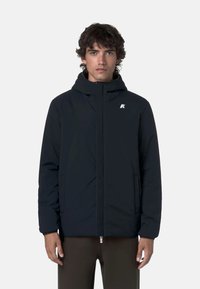 Giacca nera isolata con cappuccio, zip frontale e tasche laterali. Presenta un piccolo logo bianco sul petto. Tessuto dalla superficie liscia.