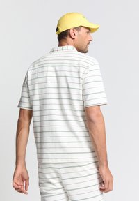 Korte mouwen, gekraagde shirt in het wit met groene horizontale strepen, met een gestructureerde stof, gecombineerd met bijpassende shorts en een gele pet.