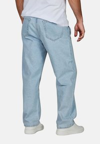 Jeans de mezclilla azul claro con un ajuste relajado, que presentan dos bolsillos traseros y detalles de costura. Llevados con zapatillas blancas.