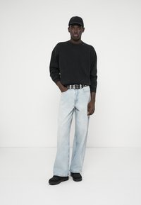 Černá mikina, světle modré široké džíny a černé boty. Doplněno o černou čepici a ozdobeno opaskem s cvočky. Jednoduché textilní textury.