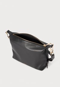 Sac à épaule en cuir noir avec une fermeture éclair dorée, une bandoulière ajustable et une texture lisse. Ouvert en haut, révélant un espace intérieur.