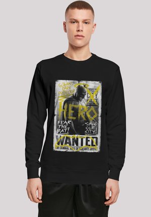 Black sweatshirt featuring a graphic print of a masked figure, with bold yellow text stating "HERO" and "WANTED." Soft, cotton fabric.