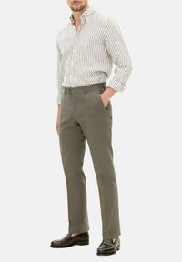 Grau gefärbte Hosen mit taillierter Passform, kombiniert mit einem weiß-grau gestreiften Hemd mit Knopfleiste. Die Schuhe sind aus dunkelbraunem Leder.
