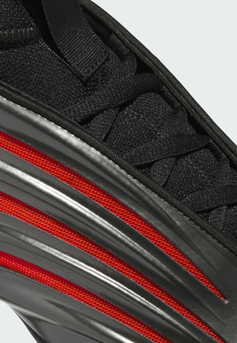 Basket noir en tissu texturé, avec des lacets élastiques et une semelle noire brillante présentant des accents en maille rouge et un design en vagues.