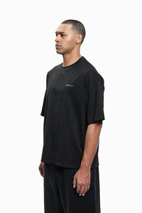 T-shirt noir à manches courtes en coton doux. Présente un col rond et un logo discret sur la poitrine. Coupe ample avec un ourlet droit.