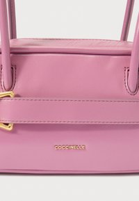 Ροζ δερμάτινη τσάντα χειρός με δομημένο σχήμα, μεταλλικά στοιχεία σε χρυσό τόνο και διακοσμητική λεπτομέρεια στον ιμάντα. Διαθέτει ανάγλυφο λογότυπο της μάρκας.