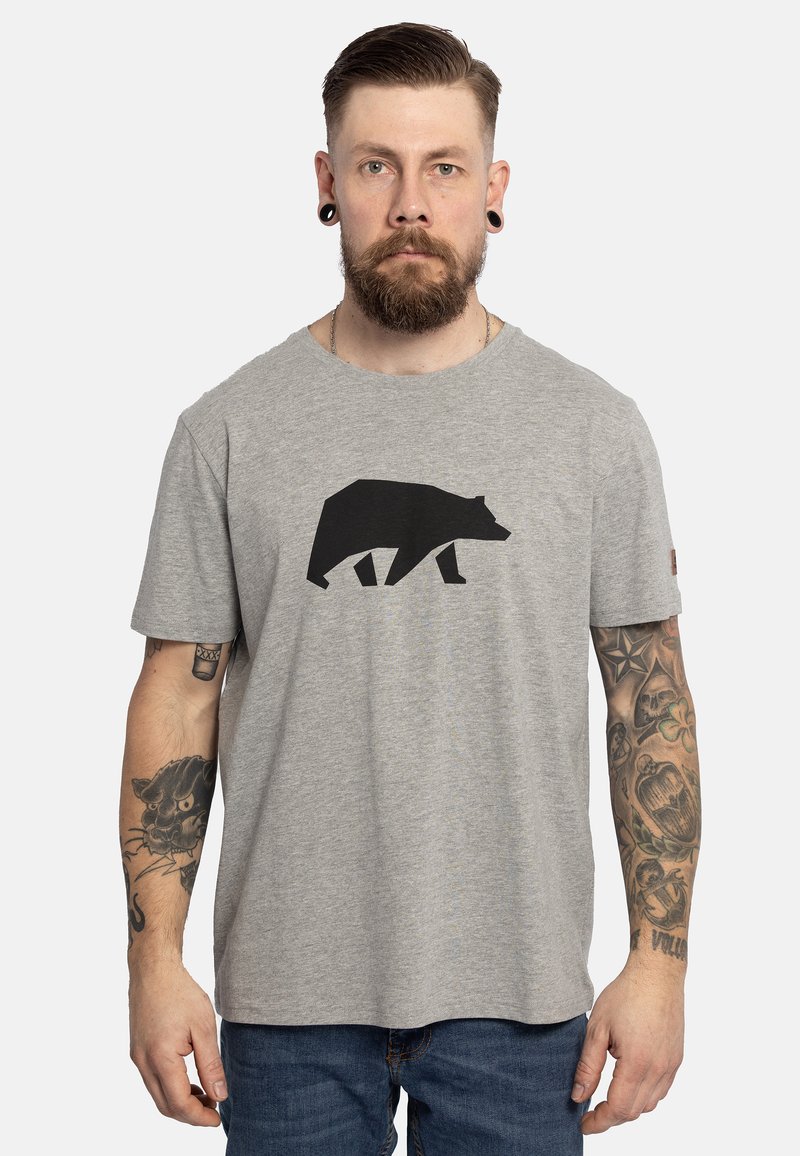 Camiseta de algodón gris con un estampado de silueta de oso negro en el frente. Mangas cortas y un corte relajado, con tatuajes visibles en el brazo.