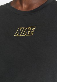 Camiseta de algodón negra con un audaz logo amarillo de "NIKE" en el centro. Diseño de cuello redondo con textura suave y forma ajustada.