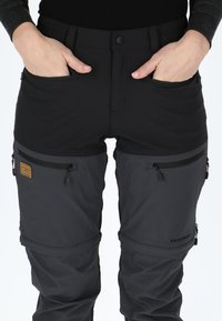 Svarta utomhusbyxor med en åtsittande design, tillverkade av ett elastiskt material. Har dragkedjefickor och en brun läderlapp med en logotyp.