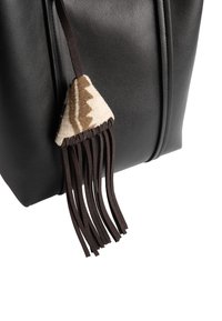 Czarna skórzana torba o fakturowanej powierzchni, z beżowym akcentem z filcu i brązowymi frędzlami, które wzbogacają jej design o charakterystyczne detale.