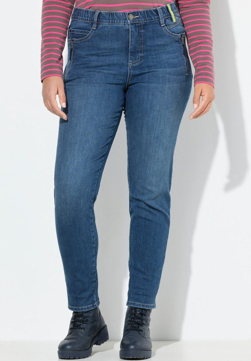 Skinny jeans i mörkblå denim med en liten glans. Har framfickor och en blixtlåsdetalj. Matchas med svarta snörstövlar.