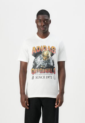 White cotton T-shirt featuring a graphic print with "ADIDAS" and "ORIGINALS," depicting a hand holding a trophy. Short sleeves and crew neck.