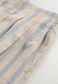 Tela de lino en beige claro con rayas verticales azules. Presenta pliegues y detalles de costura impecables, que resaltan la textura y el patrón.