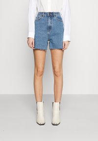 Shorts vaqueros de tiro alto en azul claro con dobladillo deshilachado, combinados con botines crema con detalles en negro y punta afilada.