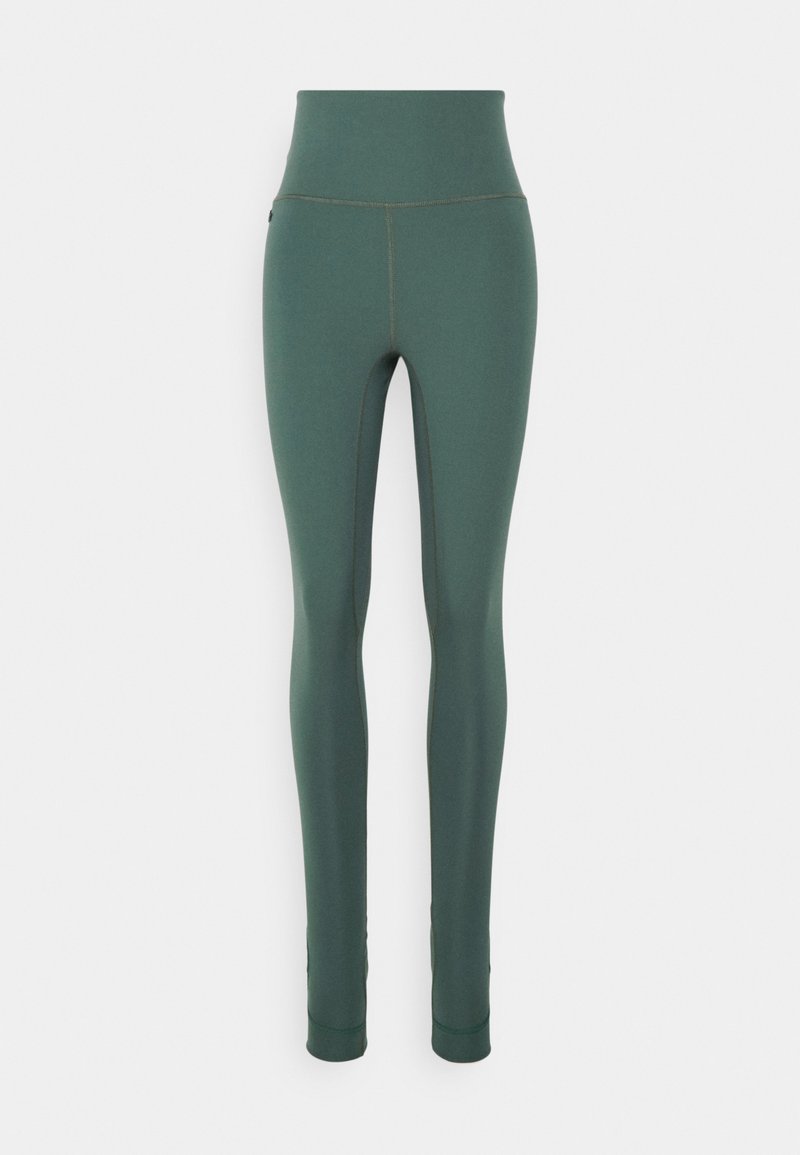 Leggings taille haute, longueur totale en tissu vert foncé avec une texture lisse et des coutures contrastées le long des coutures.