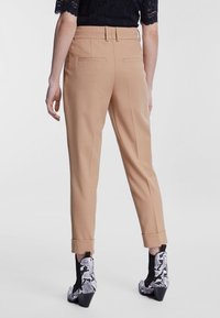 Beige skræddersyede bukser med et stilrent design, lige ben og opkrøllede nederkanter, med to baglommer. Båret med støvler med slangeskindsprint.