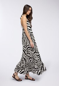 Vestito lungo a righe bianco e nero, realizzato in tessuto leggero, con orlo arricciato e spalline sottili. Abbinato a sandali neri.