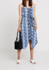 Blue snake-print dress with spaghetti straps, fitted waist, and asymmetrical hem; paired with a black woven bag and white slip-on shoes.