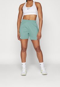 Pantalones cortos deportivos de un verde claro, hechos de una tela suave, con una cintura elástica. Combinados con un sujetador deportivo blanco y zapatillas blancas.