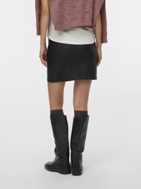 Schwarzer Jeans-Minirock kombiniert mit kniehohen schwarzen Lederstiefeln und einem rosa strukturierten Pullover, von hinten gesehen.