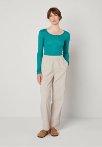 Langwijdige teal top gecombineerd met lichtbeige geribde broek. De broek heeft een elastische tailleband en zijzakken. Bruine klompen maken de look compleet.