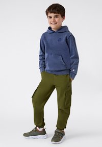 Sudadera de forro polar azul con bolsillo canguro, pantalones cargo oliva con bolsillos laterales y zapatillas grises con suelas y detalles blancos.