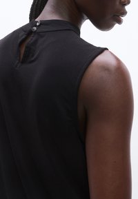 Fekete ujjatlan felső magas nyakkivágással. A hátán kulcslyuk alakú nyílás található, amit két gomb rögzít. Sima textúrájú, testhez simuló fazon.