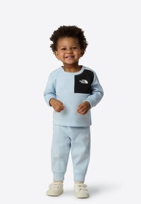 Light blue sweat set featuring a black chest pocket with logo, textured fabric, and elastic waistband on pants with cuffed hems.