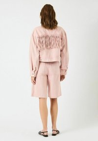 Denimjakke i pink med frynser på ryggen, parret med matchende pink shorts. Sættet har en afslappet pasform og synlige sømme.
