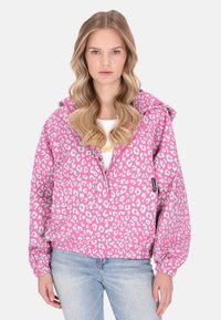 Różowa kurtka w panterkę z jasnoniebieskim wzorem, kapturem, elastycznymi mankietami i zamkiem błyskawicznym. Połączona z jasnoniebieskimi jeansami.